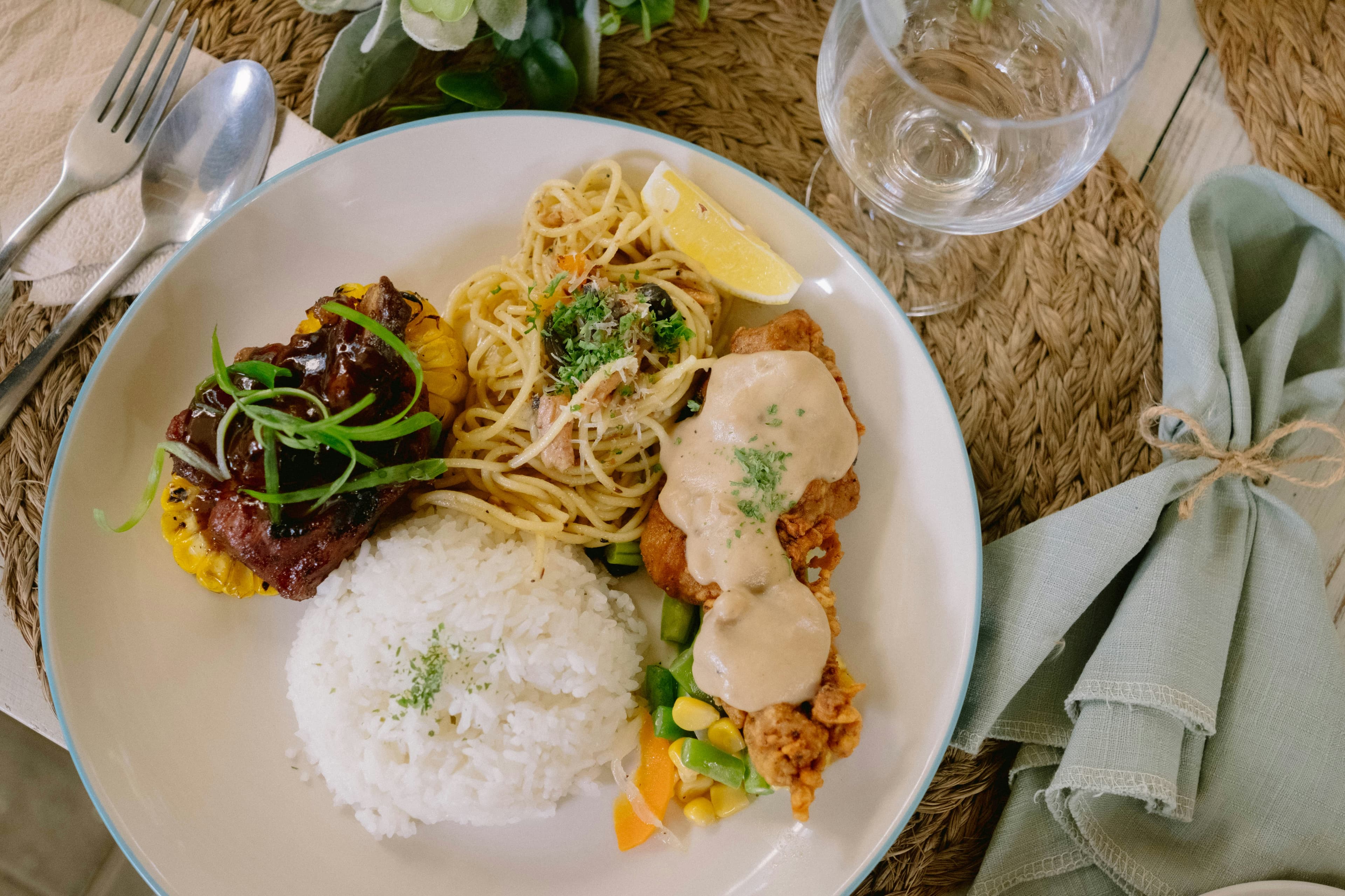 A traditional Polynesian-style plate with rice, mixed vegetables, glazed protein, and noodles served on woven raffia